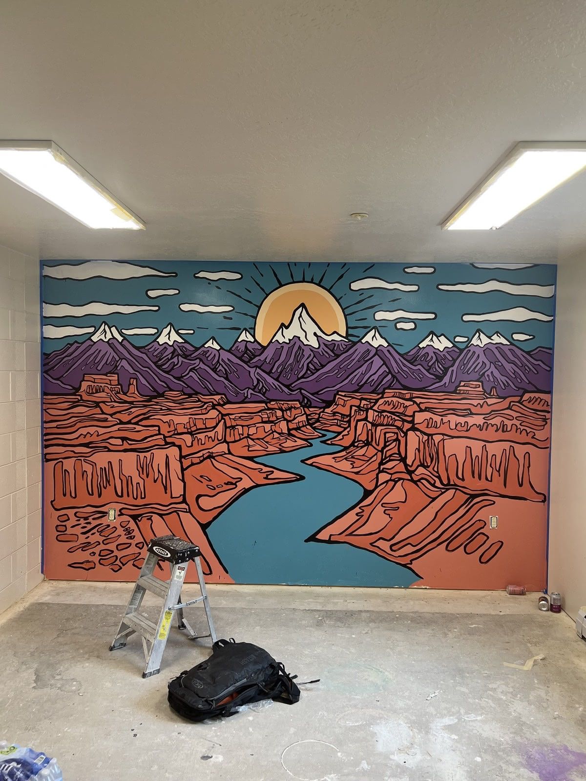 Painted wall of a red desert river canyon below purple peaks and a rising sun