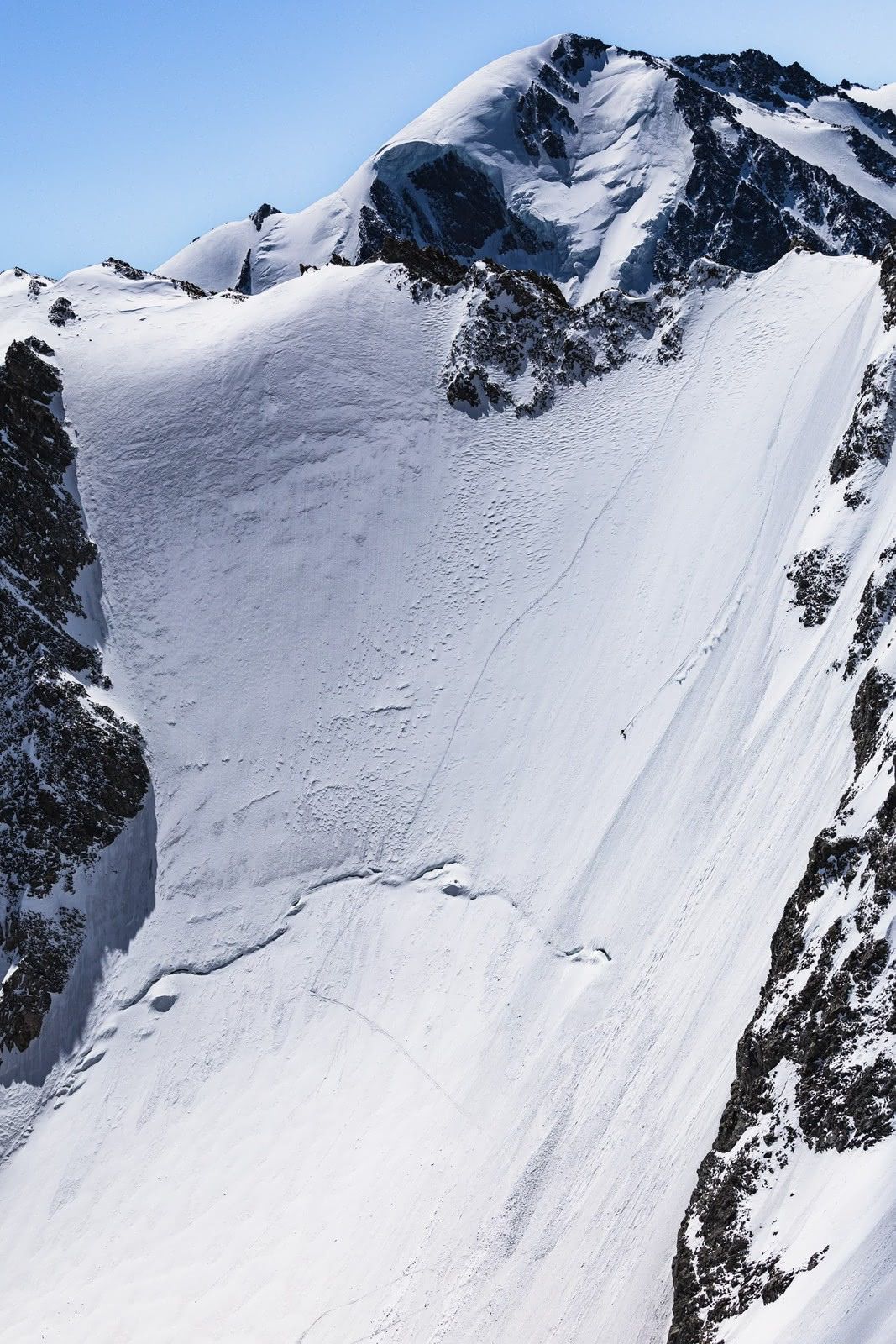 Tiny skier tracking a huge sunlit alpine face